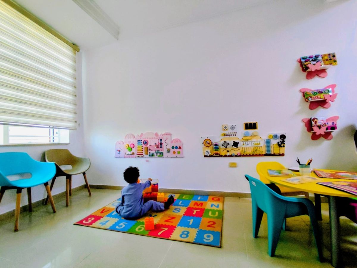 Salle d'attente avec coin jeux : tapis alphabet, tableaux d'éveil muraux et petite table d'activités